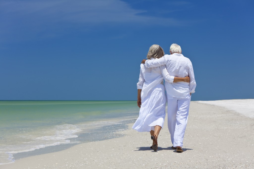 Rear View Of Senior Couple Walking Alone On A Tropical Beach